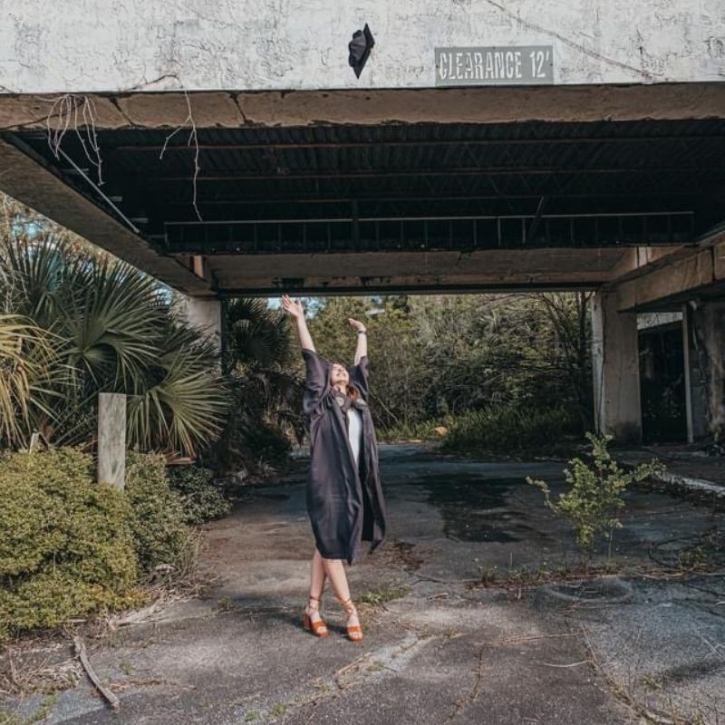 Graci Williams throws her grad cap in the air in front of a bridge.