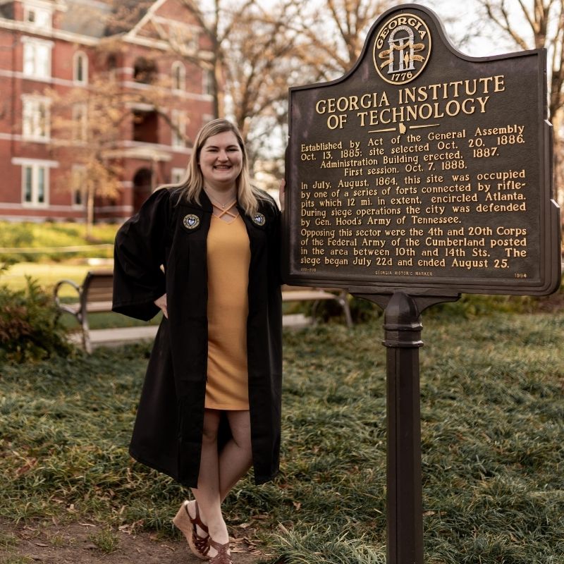 Headshot of Amelia Rousseau in graduation regalia in front of the Georgia Tech incorporation sign.