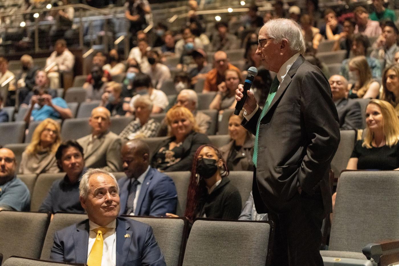 Sam Nunn holds a microphone and stands in a crowd to ask a question.